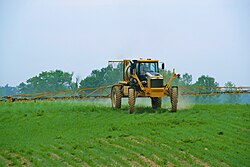 A row-crop sprayer applying pesticide to a young crop of maize