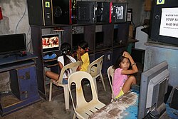 An Internet café in Cebu City, Philippines. A partially out of sight paper signage forbidding profanity is seen on the right, while two girls in the background are watching a depiction of the Flagellation of Christ.