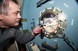 Pavel Vinogradov looks out of a Poisk hatch window at Alexander Misurkin on EVA.