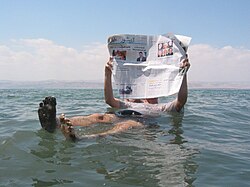 A person floating because of the highly saline water, with no need to swim to stay afloat reading a newspaper in the water is popular tourist photo setup