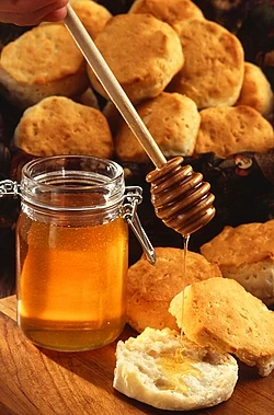 A jar of honey with a dipper and a biscuit