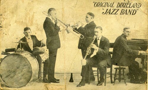 The Original Dixieland Jazz Band, from the original 1918 promotional postcard while the band was playing at Reisenweber's Cafe in New York City. Shown are (left to right) Tony Sbarbaro (a.k.a. Tony Spargo) on drums; Edwin "Daddy" Edwards on trombone; D. James "Nick" LaRocca on cornet; Larry Shields on clarinet, and Henry Ragas on piano.