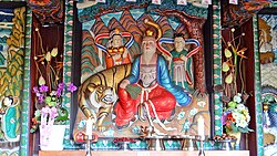 An altar depicting several human figures and a tiger with flowers and candles