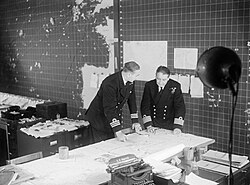 Staff officers discuss convoy movements in the Operations Room at the Western Approaches Command headquarters, Derby House, in Liverpool, England, during World War II, in September 1944.