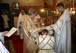 Eastern Orthodox subdeacon being ordained to the diaconate. The bishop has placed his omophorion and right hand on the head of the candidate and is reading the Prayer of Cheirotonia.
