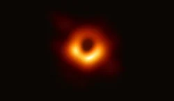 Over a black background of empty space, an orange-red donut of gas lies in the center of the image, with a black circle--the black hole's shadow--in the middle of the donut.