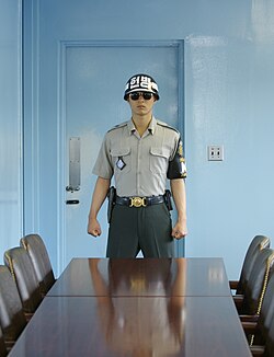 A Republic of Korea soldier of the United Nations Command Security Battalion stands guard inside a JSA conference room, in front of the door leading to the North Korean side of the JSA. View from south to north.