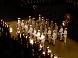21 cadets in white uniforms perform a salute with a rifle