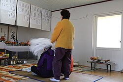 Two people on a mat, one sitting and the other standing behind them