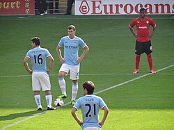 The Edin Džeko (blue, no. 10) and Sergio Agüero (no. 16) duo for Manchester City (2011–2015) is a recent example of a striker partnership made up of a taller and more physically imposing player combined with a shorter and technically gifted partner.[70]