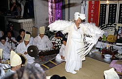 A person dressed entirely in white performing a ritual among other sitting persons