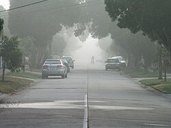 Light fog reduces visibility on a suburban street, rendering the cyclist very hazy at about 200 m (220 yd). The limit of visibility is about 400 m (440 yd), which is before the end of the street.