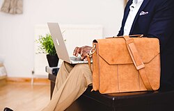 Light-brown leather bag next to man typing on laptop