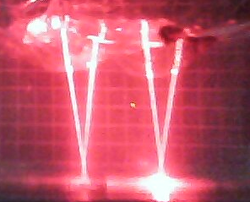 Two horse lenses suspended on water by cling wrap with four approximately parallel lasers directed through them. The 1 cm spaced grid indicates a near focus focal length of around 6 cm.