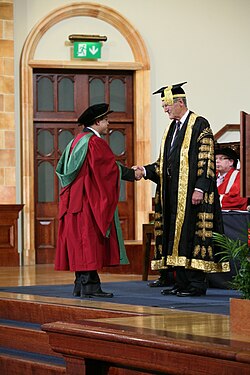 A new PhD graduate from the University of Birmingham, wearing a doctor's bonnet, shakes hands with the chancellor.