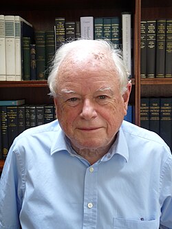 Photo of a man with white hair wearing a blue shirt.