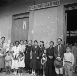 Relatives of victims killed in the Ponce massacre. Machine gun bullet holes are visible in the wall. (Ponce, Puerto Rico)