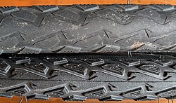 Two tires of the same make and tread pattern, the lower one completely unused, the upper one has rolled over 1,500 km (900 mi) on varying surfaces.