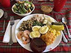 A Thanksgiving dinner with roast turkey, mashed potatoes, pickles, corn, candied yams, cranberry jelly, shrimps, stuffing, green peas, deviled eggs, green salad, and apple sauce