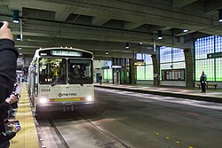 A cream-colored bus in a station within a tunnel, being photographed by transit fans