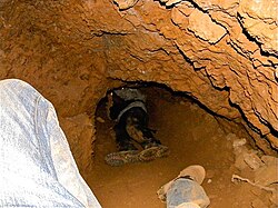 Interior of an artisanal mine near Low's Creek, Mpumalanga Province, South Africa. The human figures, exploring this mine, show the scale of tunnels driven entirely with hand tools (two-kilogram (4.4 lb) hammer and hand-forged scrap-steel chisel).