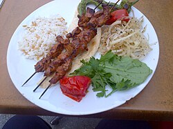 Şiş kebap with "şehriyeli pilav" (orzo pilaf), onions with sumac, a grilled pepper, a slice of tomato (also grilled) and rucula leaves
