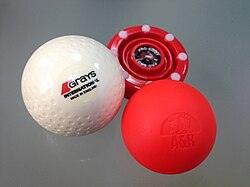 An assembly of field hockey balls and a roller hockey puck