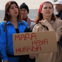 In Hatay, Turkey, two women hold a sign that says 'Mara Haya Hurriya', meaning 'Woman, Life, Freedom' in Levantine Arabic. The phrase is written using the Latin-based Turkish alphabet.
