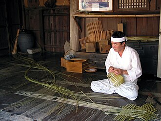 A man in hanbok, traditional Korean costume weaving a basket in Yangdong village